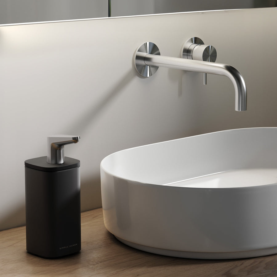 Simplehuman Matte Black 10 oz. Pulse Pump on a wooden bathroom vanity beside a white vessel sink.