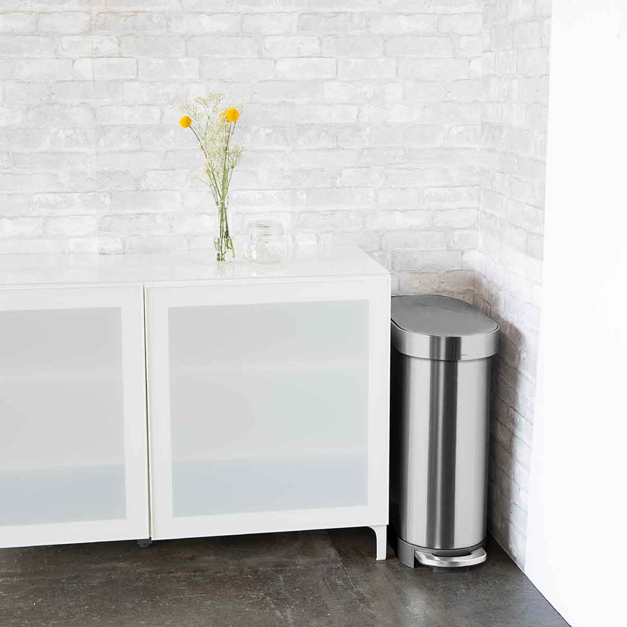 Simplehuman 45L Slim Step Can in Brushed Stainless Steel placed tightly against wall and cabinet, hands-free operation.