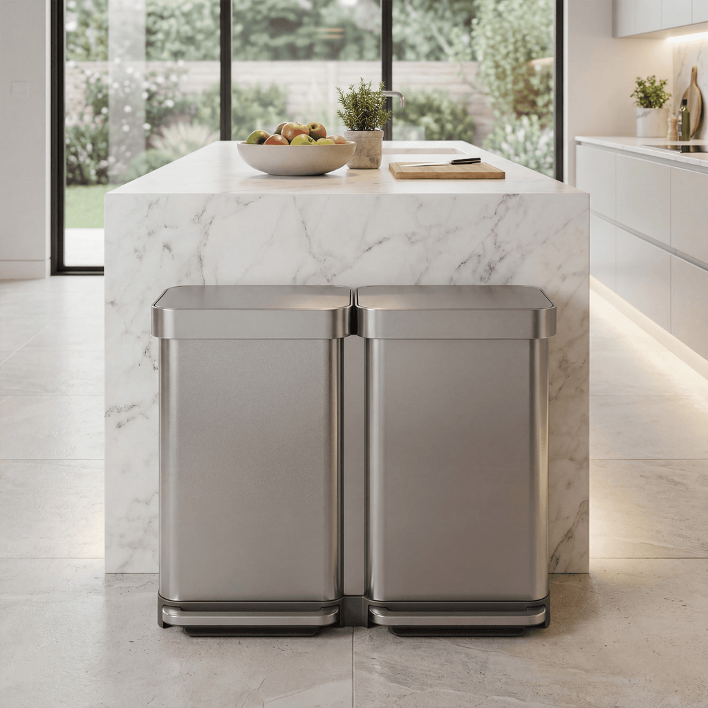 Simplehuman's 90L Step Recycler in Brushed in a modern contemporary kitchen with white counters and a marble island in the center of the kitchen with fruits, plants, and a cutting board on top. The image focuses on the can in the center.