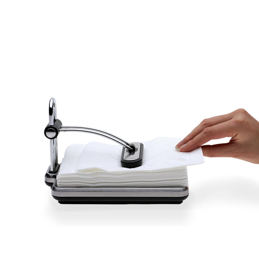 Usage view, Simplehuman Quick Grip Napkin Holder in Polished Stainless Steel, hand pulling single napkin while weighted arm secures stack.