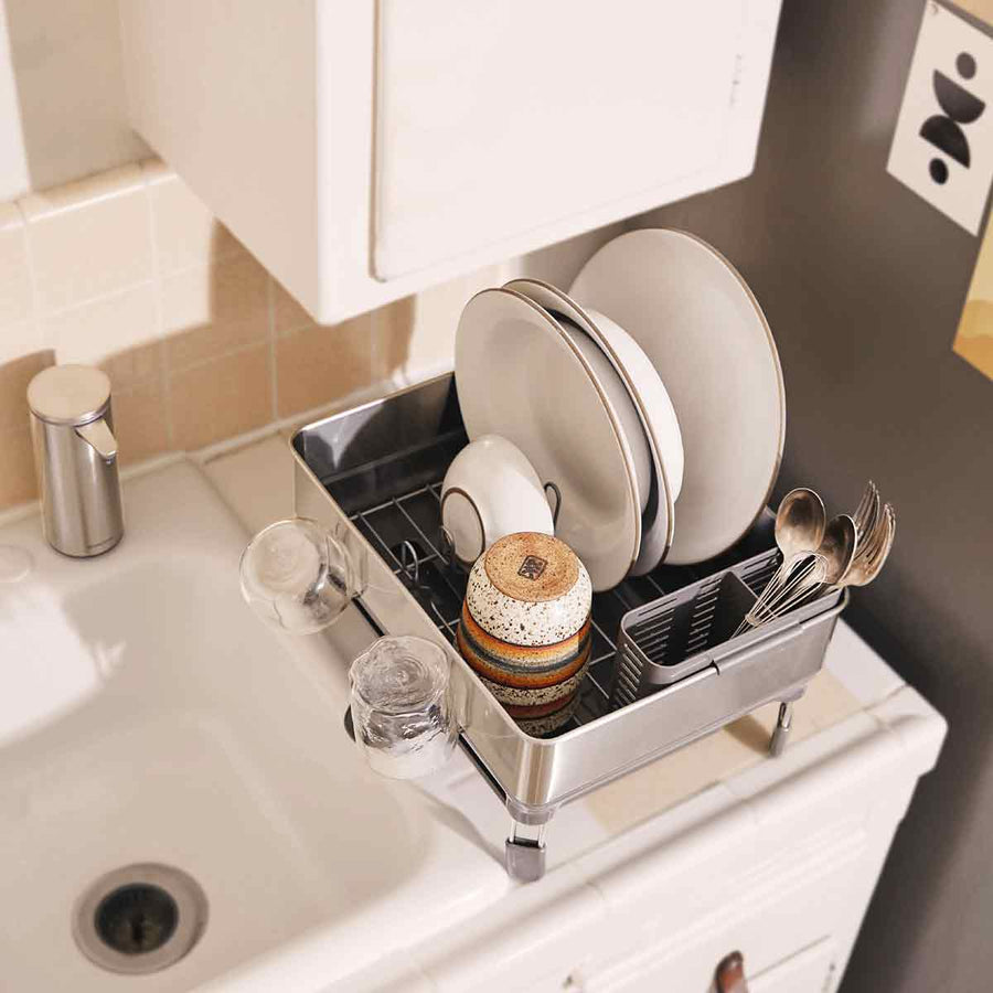 High-angle lifestyle view of Simplehuman Compact Steel Frame Dishrack in Brushed Stainless Steel, actively drying dishes next to sink.