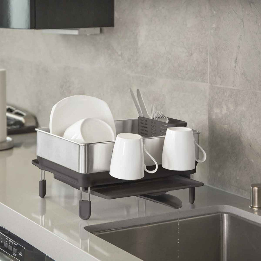 Lifestyle view of Simplehuman Compact Brushed Steel Dishrack on counter with adjustable spout draining into sink.