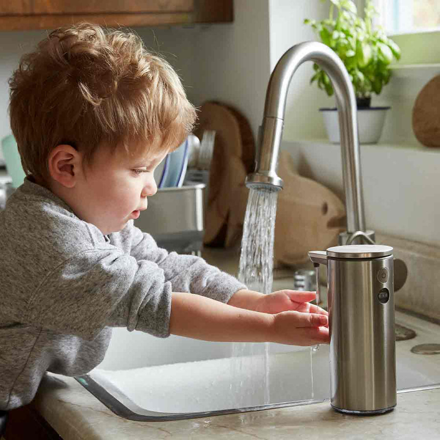 Simplehuman 9 oz. Rechargeable Sensor Pump in Brushed Stainless Steel, used by child washing hands at kitchen sink, touch-free.