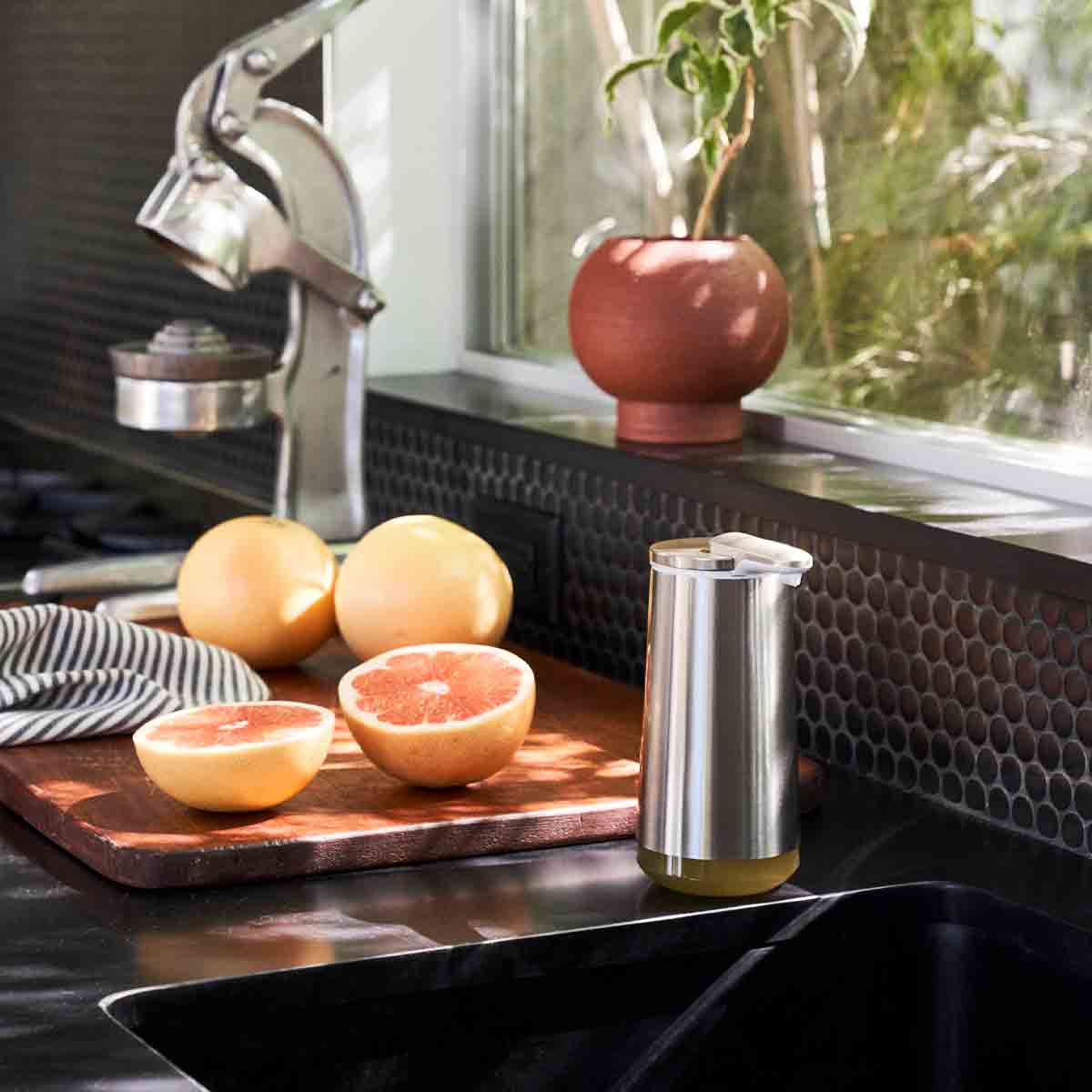 Lifestyle view of Simplehuman Brushed Stainless Steel Foam Sensor Pump by a kitchen sink and cutting board, touch-free foaming soap.