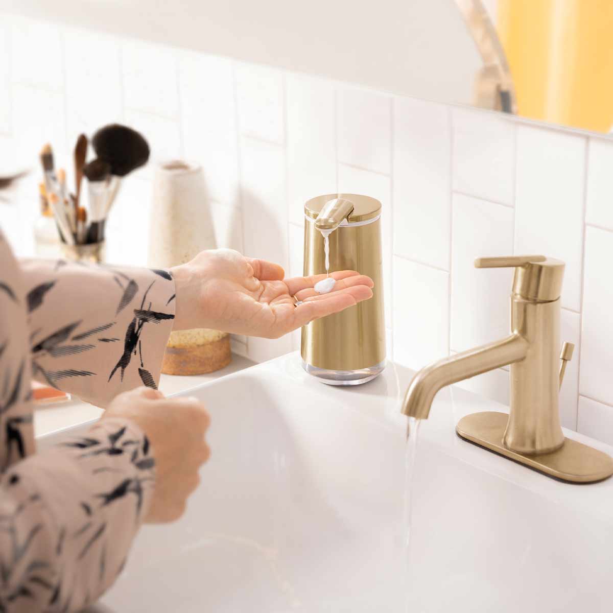 Lifestyle view of Simplehuman Brass Foam Sensor Pump dispensing foam into a hand over a bathroom sink.