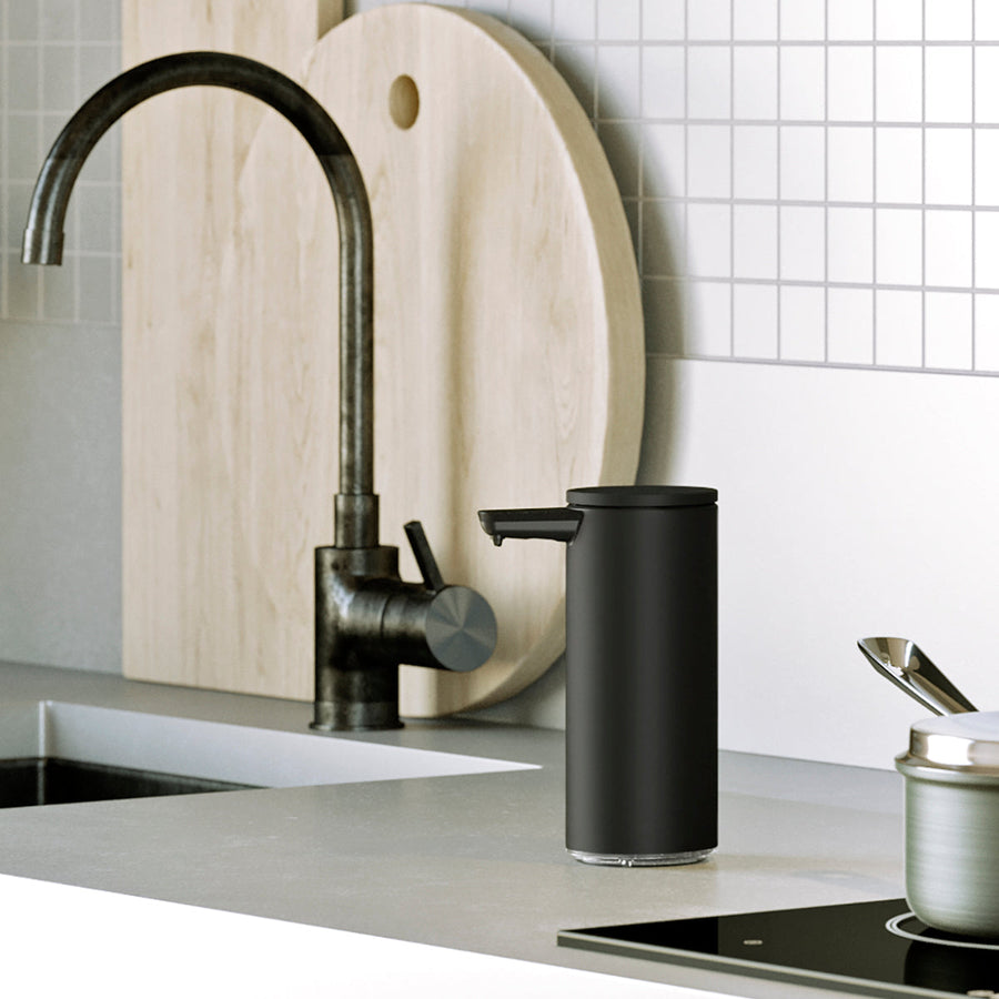 Lifestyle view of Simplehuman 9 oz. Rechargeable Sensor Pump in Matte Black on a kitchen sink countertop, hands-free.