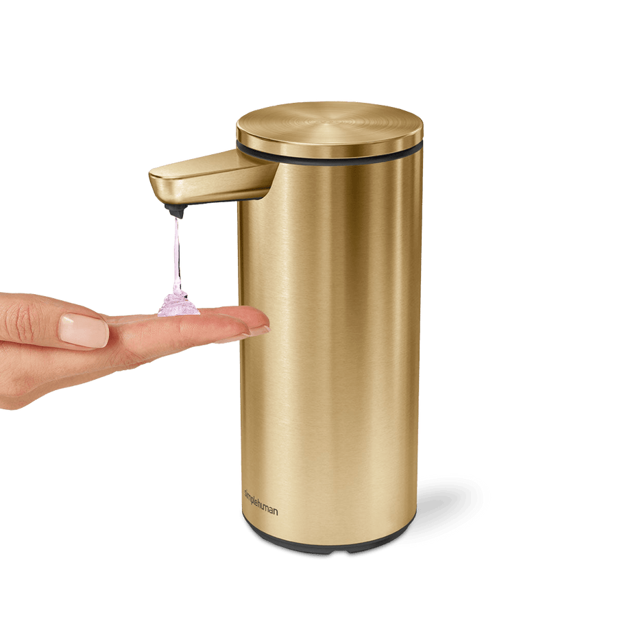 Action view of Simplehuman 9 oz. Rechargeable Sensor Pump, Brass, dispensing soap onto hand, touch-free operation.