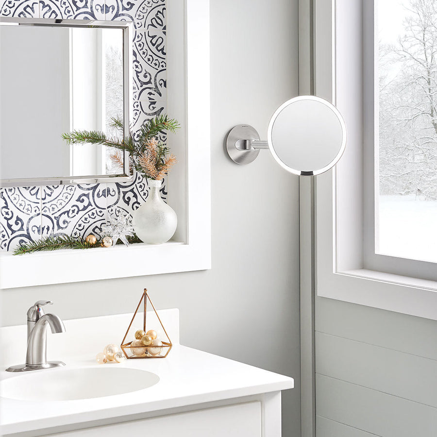 Simplehuman Rechargeable Wall Mount Sensor Mirror in Brushed Stainless Steel, extended over a vanity counter, hands-free lighting.