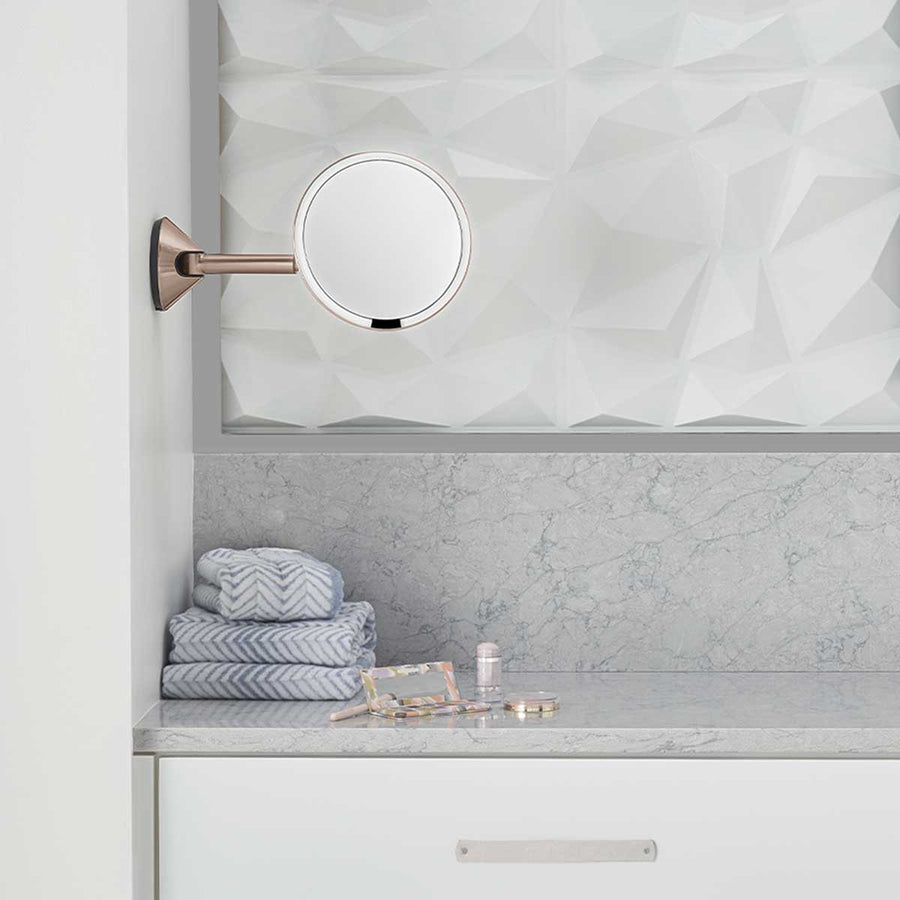 Simplehuman Rose Gold Wall Mount Sensor Mirror over a vanity counter, rechargeable and adjustable arm.