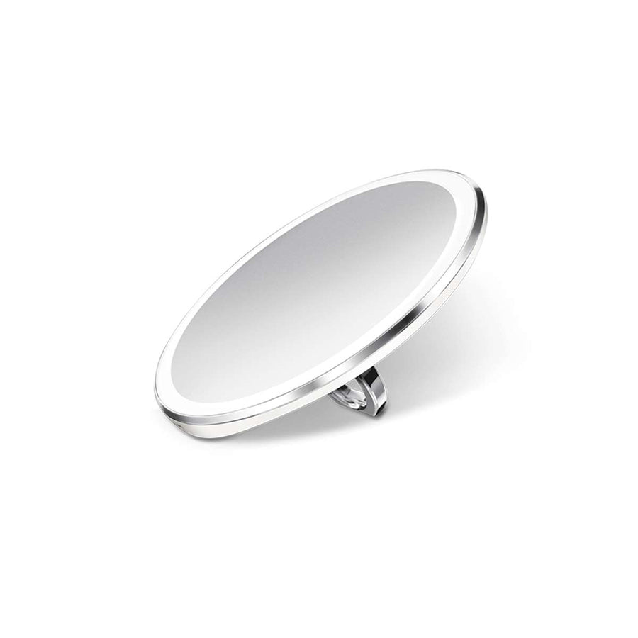 Angled studio view of Simplehuman Sensor Mirror Compact 3x, Brushed Stainless Steel, illuminated, hands-free.
