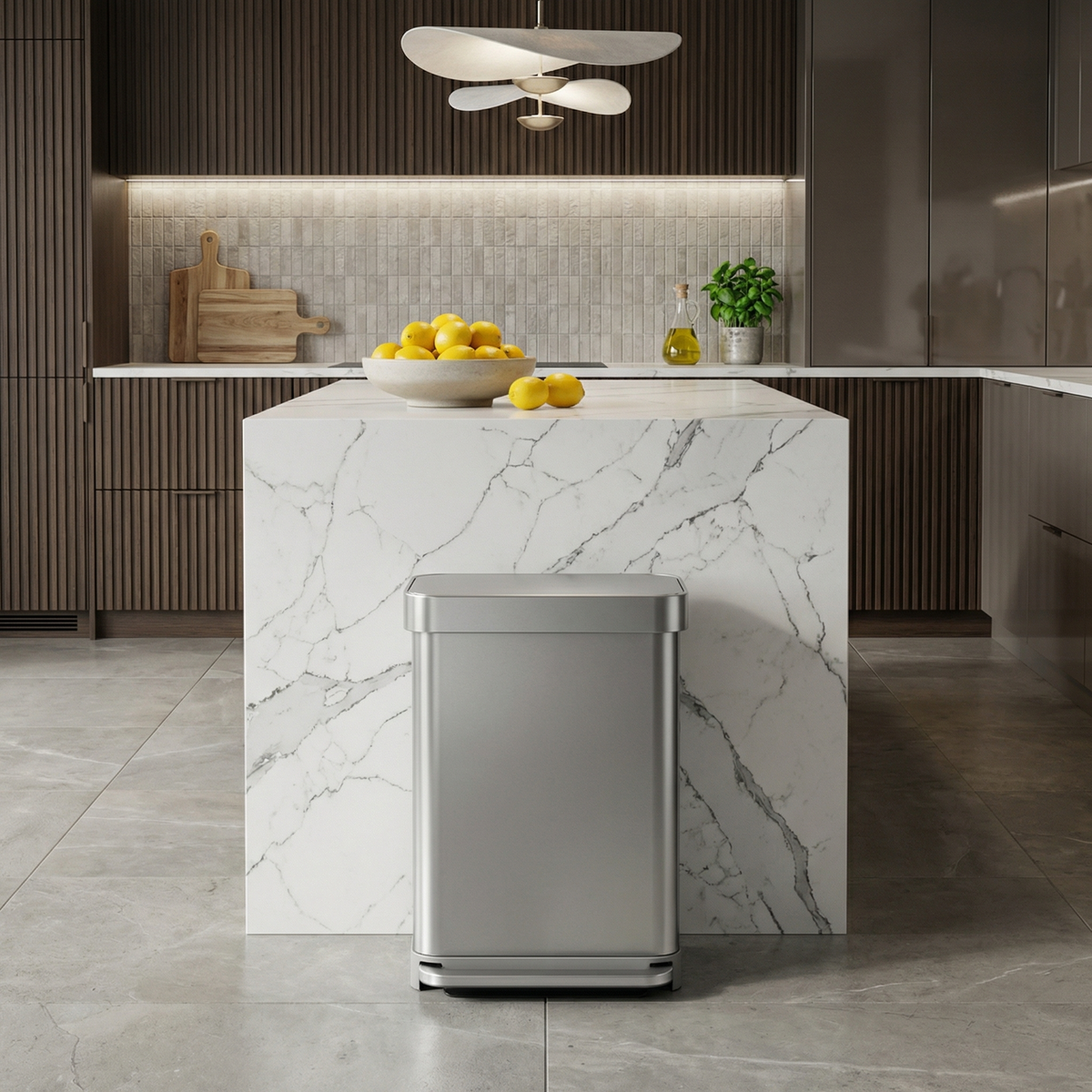 Simplehuman's 55L Step Can in Brushed in a modern kitchen setting with modern appliances and along a marble center countertop.