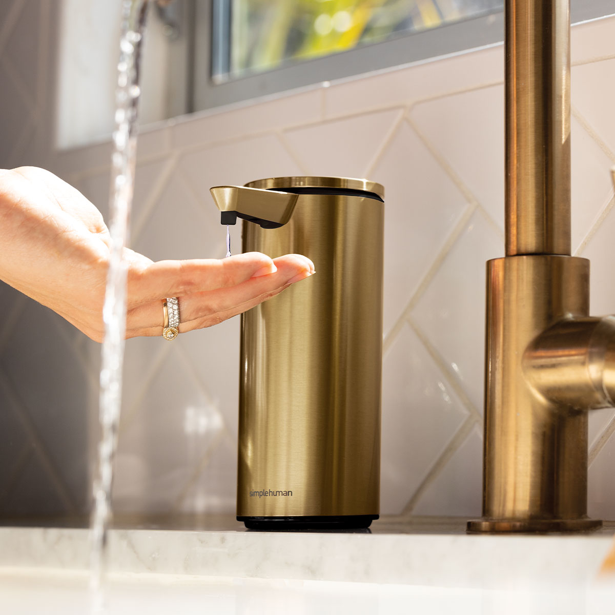 Angled view of Simplehuman Fragrance Free Liquid Hand Soap being used with a Brass sensor pump dispenser, touch-free operation.