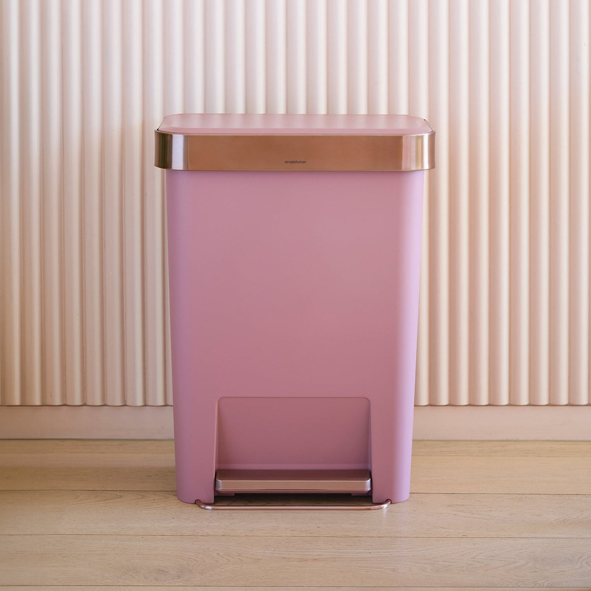 Simplehuman's 45L Hybrid Step Can in Blush on wooden floor with vertical tiles in background.